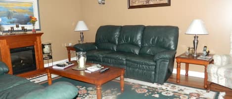 A living room with a green leather sofa, a wooden coffee table, a fireplace, and a floral rug.