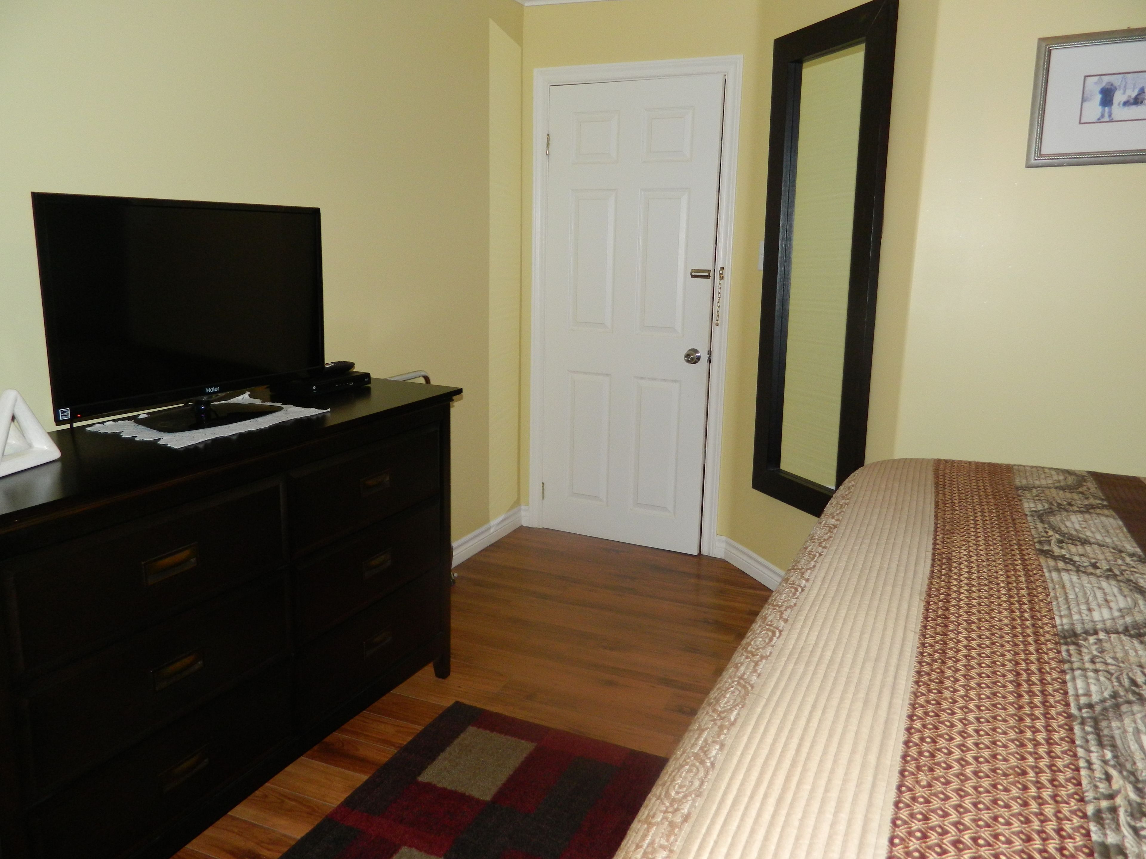 A bedroom with a bed, a dresser, a television, and a door.