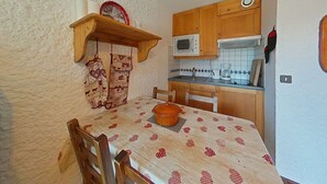 Une petite cuisine avec des meubles en bois, un four à micro-ondes, une machine à café et une table recouverte d’une nappe à motifs.