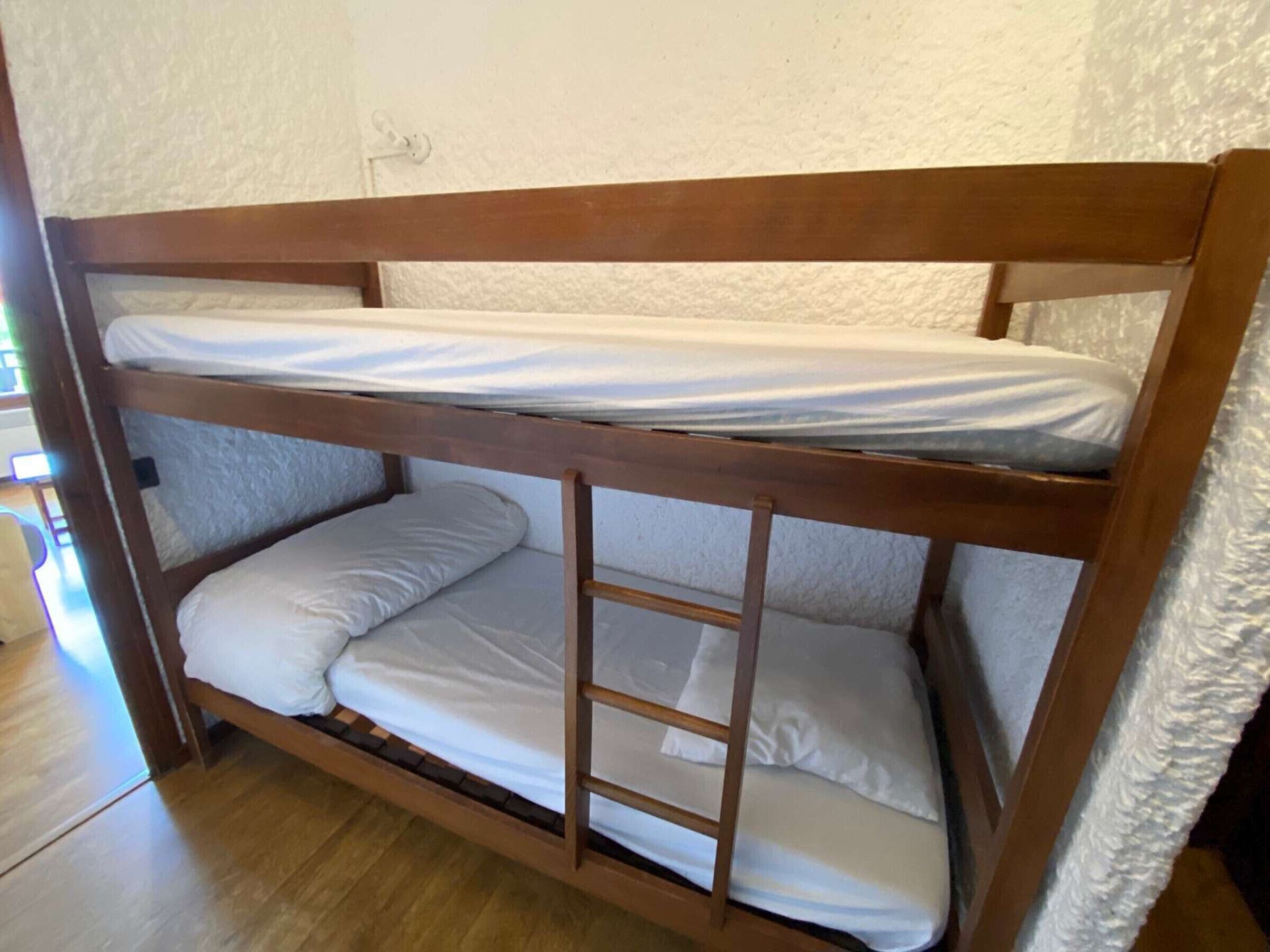 A bunk bed with two levels, wooden frame, and white bedding.