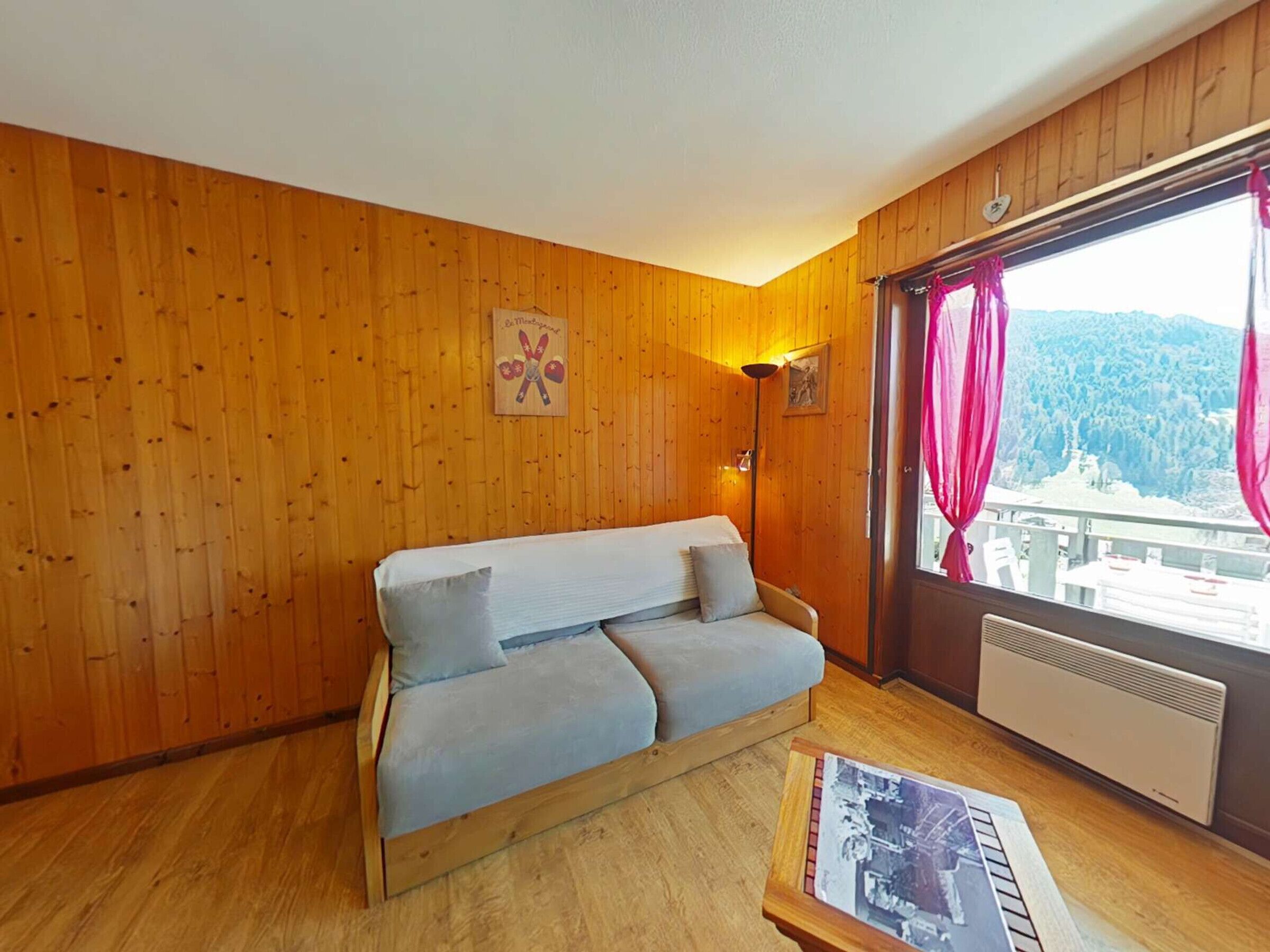 Ett rum med träpanel på väggarna, en soffa, en inramad tavla och ett fönster med gardiner.