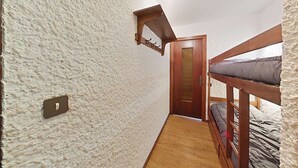 Une petite pièce étroite, avec un lit superposé, une porte en bois et un mur à la texture particulière.