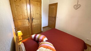 A bedroom with a wooden wardrobe, a bed with striped pillows, and a heart-shaped decoration on the wall.