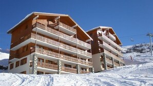 A multi-story hotel with balconies and a ski lift in the background.
