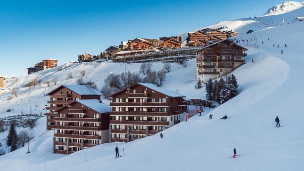 A ski resort with multiple wooden buildings, ski slopes, and skiers.
