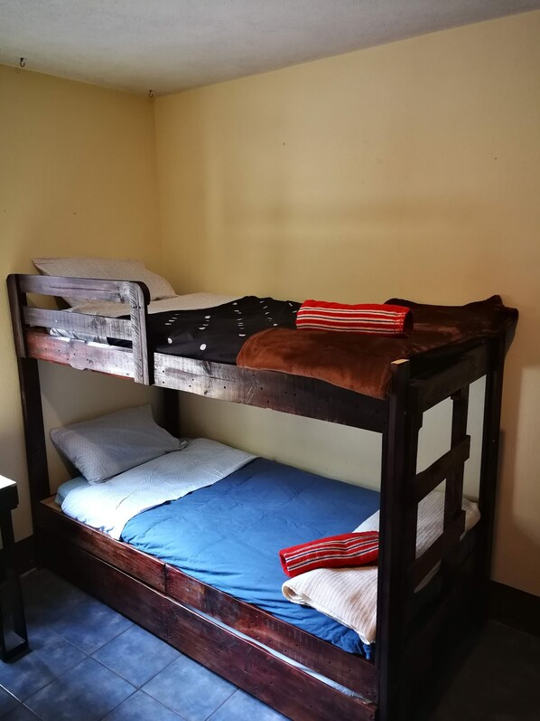 A bunk bed with two levels, a small bedside table, and a plain wall. - Casa I'X - Hostel (Quetzaltenango)