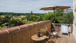 Un balcón con vistas al campo, una mesa con un florero y dos sillas.