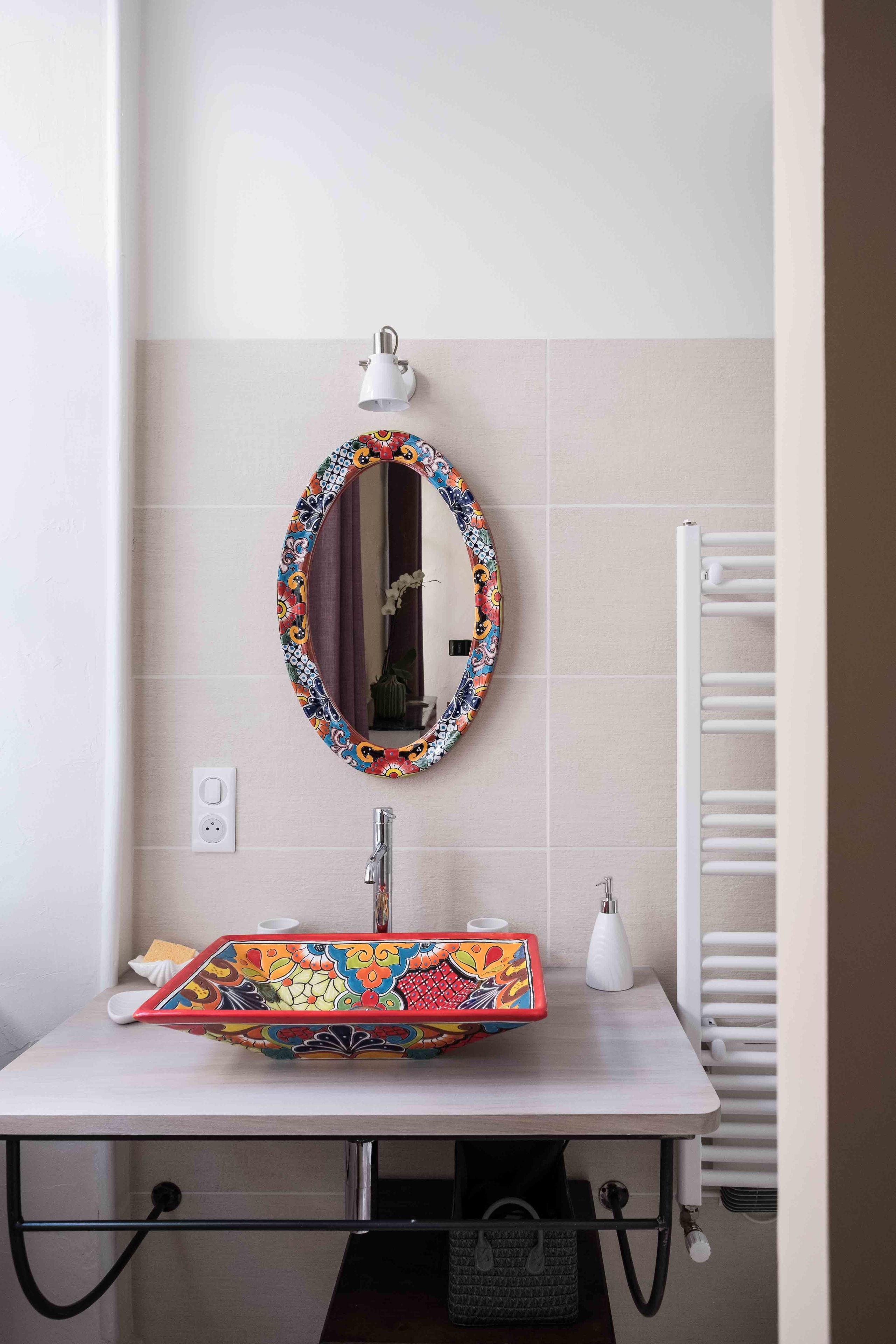 Un baño con un lavamanos blanco, un espejo colorido y un perchero blanco.