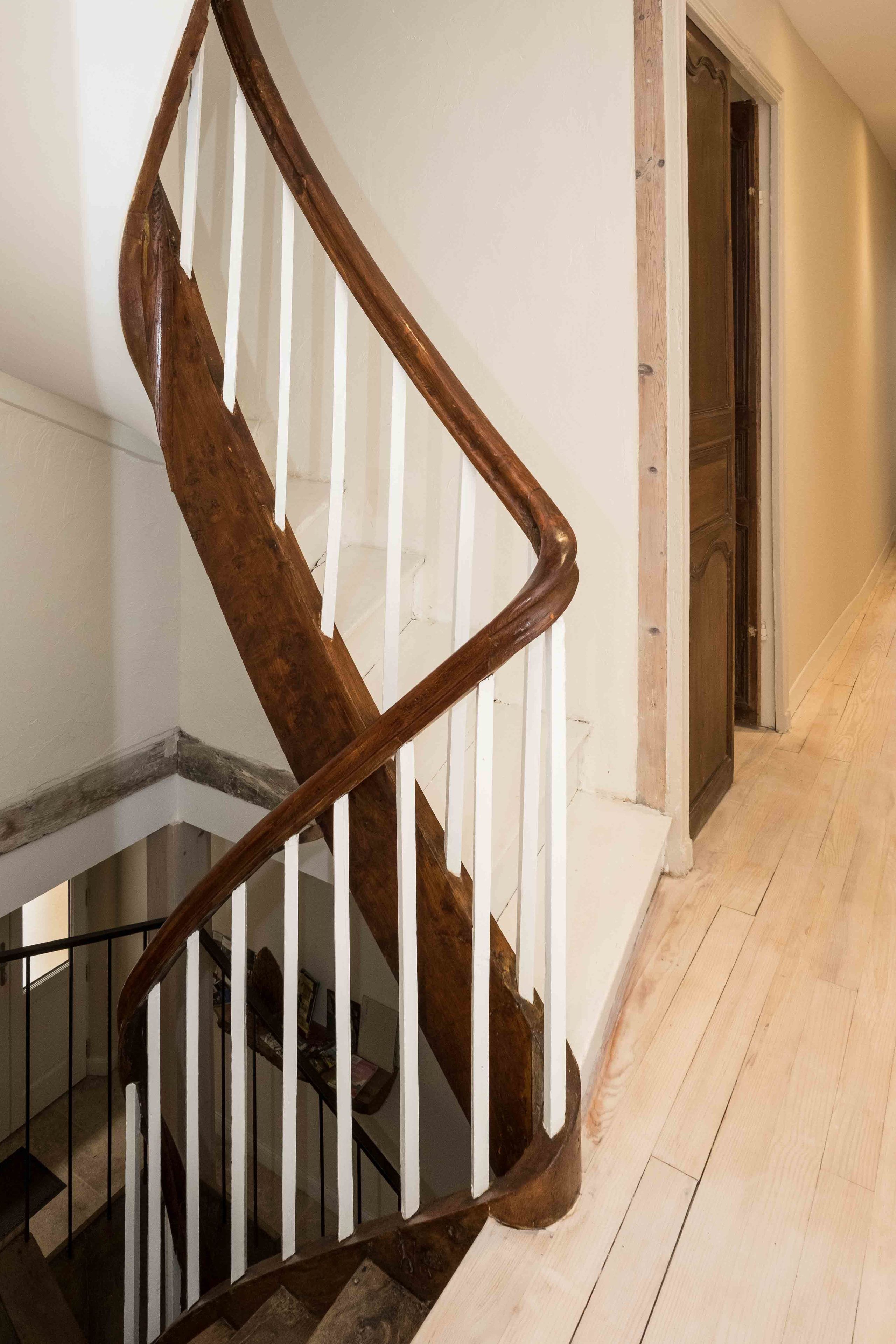 A wooden staircase with white balusters and a dark wooden handrail.