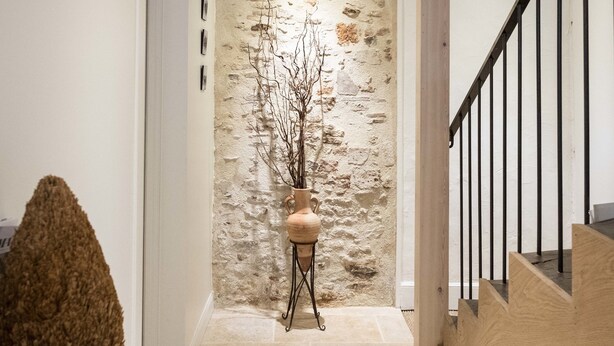 Un pasillo con pared de piedra, escalera de madera y un jarrón decorativo.