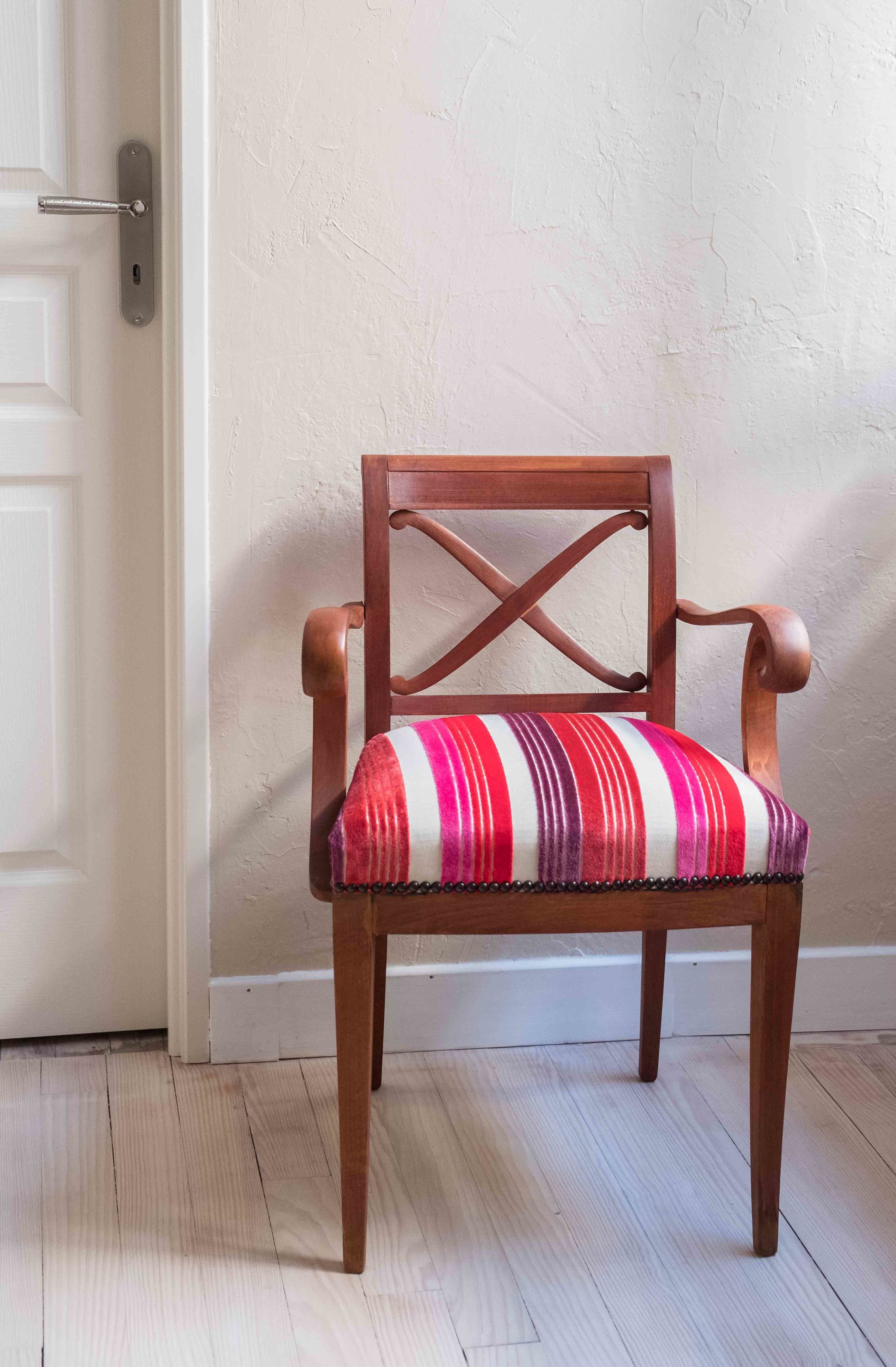 A wooden chair with a striped cushion in a room with a white door and textured walls.