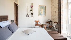 Un dormitorio con cama, una silla, una mesita y un cuadro en la pared.