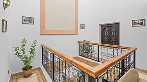 A staircase with a wooden handrail and black metal balusters, leading to a landing with a potted plant and a door with intricate metalwork. - Riad Marwa (Marrakech)