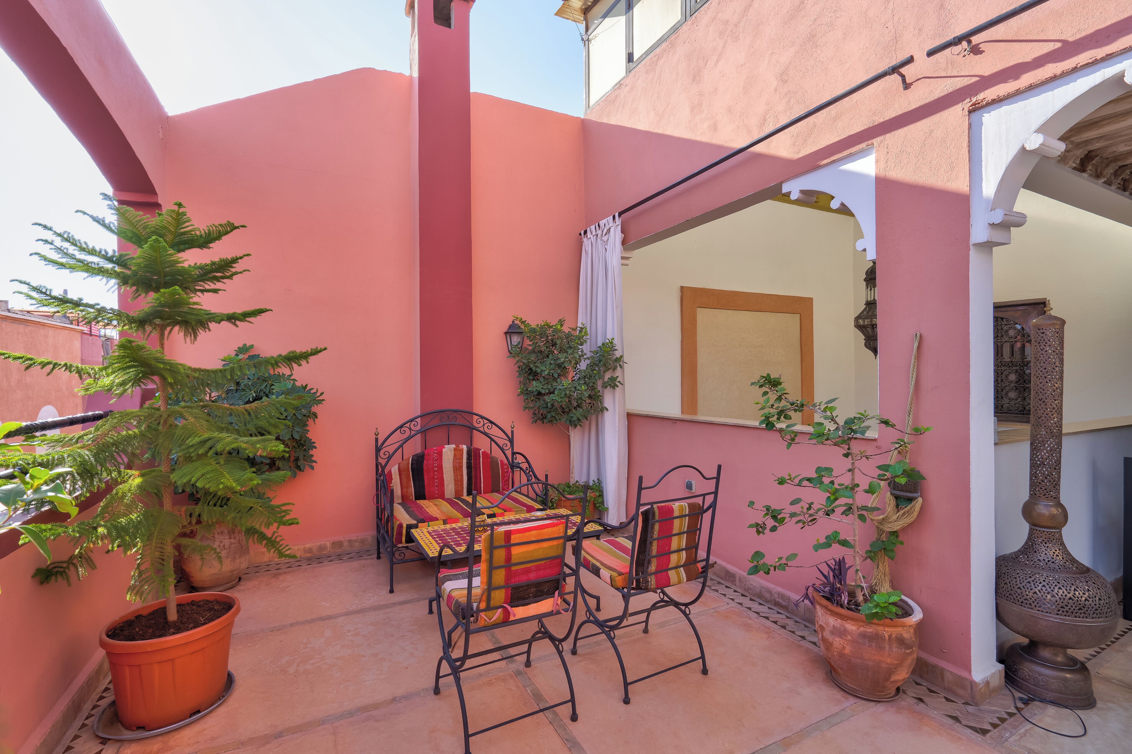 An outdoor patio with a table and chairs, surrounded by potted plants and a decorative lamp.