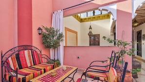 A cozy outdoor seating area with a metal table and chairs, a colorful striped sofa, and a potted plant. - Riad Marwa (Marrakech)