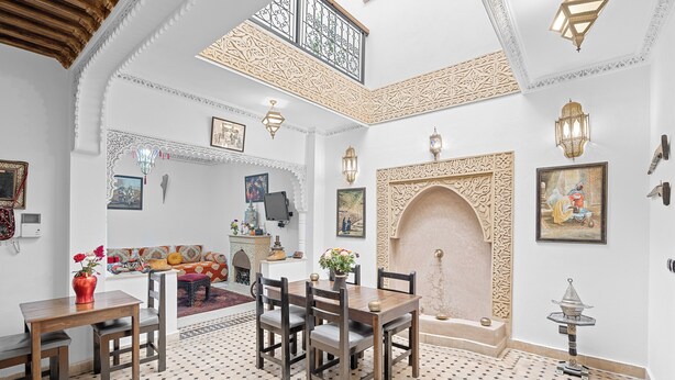 A dining area with a wooden table and chairs, surrounded by ornate wall decorations and a patterned floor. - Riad Marwa (Marrakech)