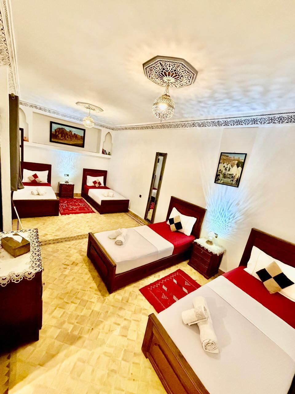 Una habitación de hotel con dos camas, alfombra roja, suelo de madera, candelabro y espejo.