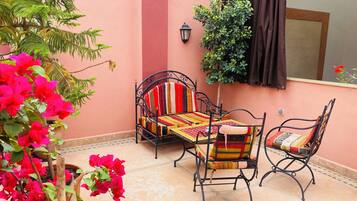 A patio with a metal-framed sofa, a small table, and chairs, surrounded by potted plants and flowers.