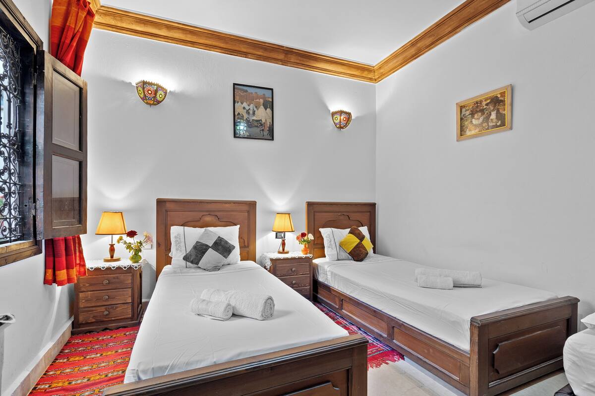 A hotel room with two single beds, wooden headboards, a red patterned carpet, and a wooden ceiling.
