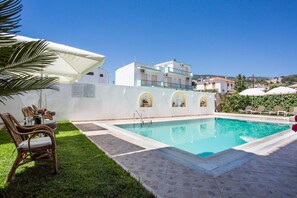 A swimming pool with a tiled deck, a table with chairs, and a white umbrella. - Studios Ritsa (Skiathos)