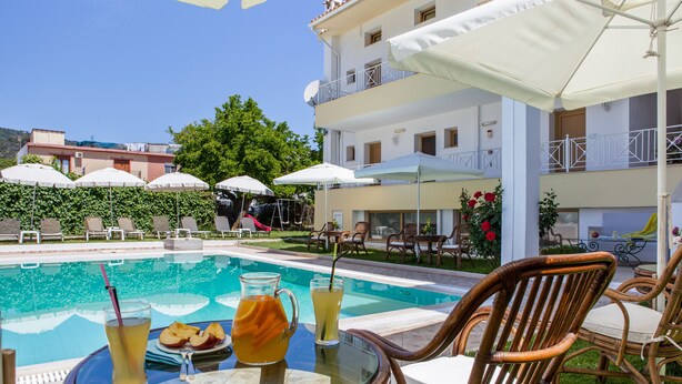 Zona junto a la piscina con sillones, sombrillas y una mesa con bebidas y aperitivos.