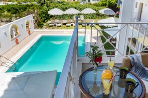 A poolside area with a glass table, lounge chairs, and umbrellas. - Studios Ritsa (Skiathos)