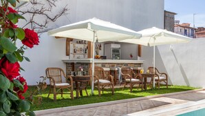 Zona junto a la piscina con bar, asientos exteriores y piscina con azulejos.
