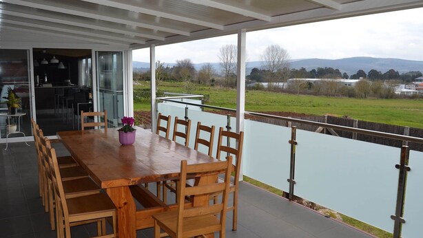 A covered dining area with a wooden table and chairs, a potted plant, and a view of a lake and hills. - Albergue Alfonso II el Casto - Hostel (Melide)