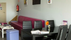 A modern waiting area with a red sofa, black chairs, a small table with a book and a flower vase, and a fire extinguisher on the wall. - Albergue Alfonso II el Casto - Hostel (Melide)