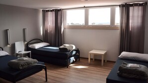 A hotel room with two single beds, a small table, and a window with curtains. - Albergue Alfonso II el Casto - Hostel (Melide)