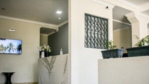 A reception area with a marble reception desk, a TV mounted on the wall, and a potted plant. - Pousada Espaço Viana (Ipojuca)