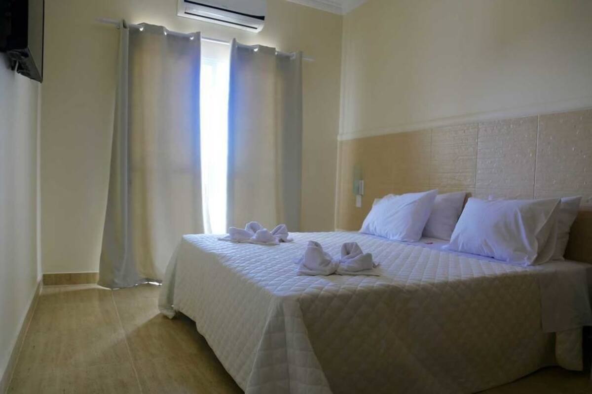 Une chambre d’hôtel avec un grand lit, du linge de lit blanc, une table de chevet et une fenêtre avec des rideaux.