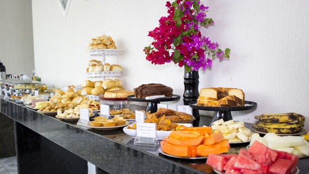 A buffet with various food items and a vase of flowers. - Pousada Espaço Viana (Ipojuca)