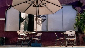 A poolside area with a table and chairs, an umbrella, and a building with a large sign. - Pousada Espaço Viana (Ipojuca)