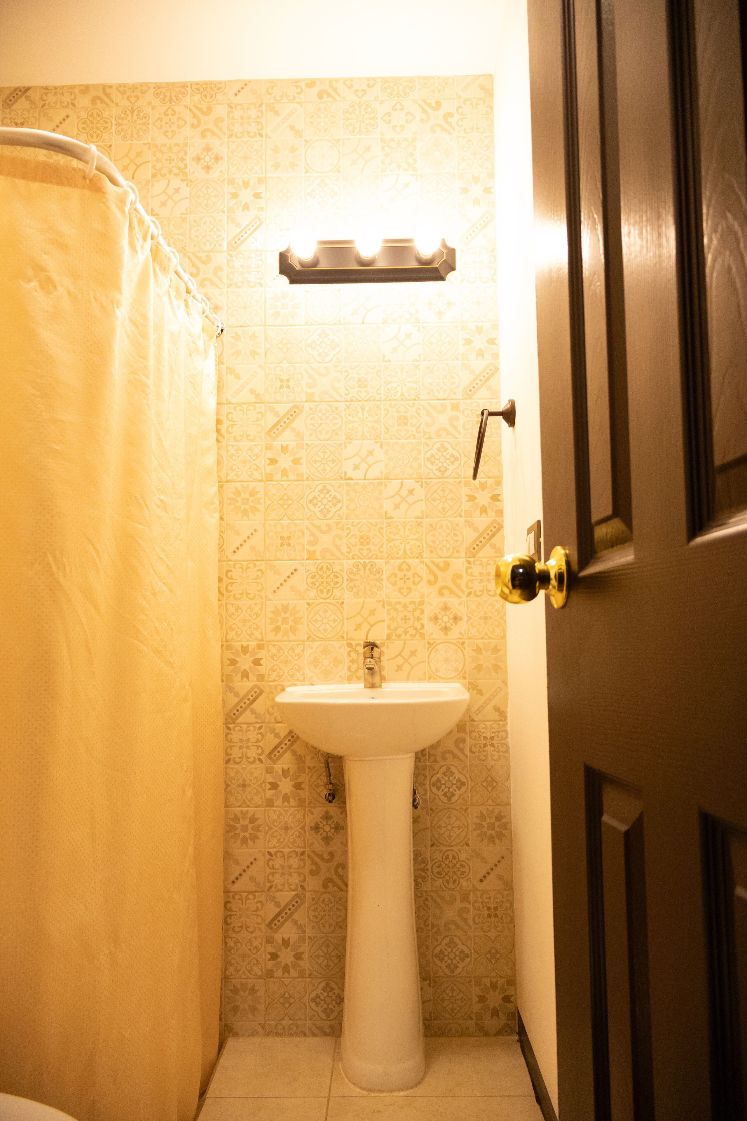 A bathroom with a white sink, patterned tiles, a shower curtain, and a door with a brass handle.