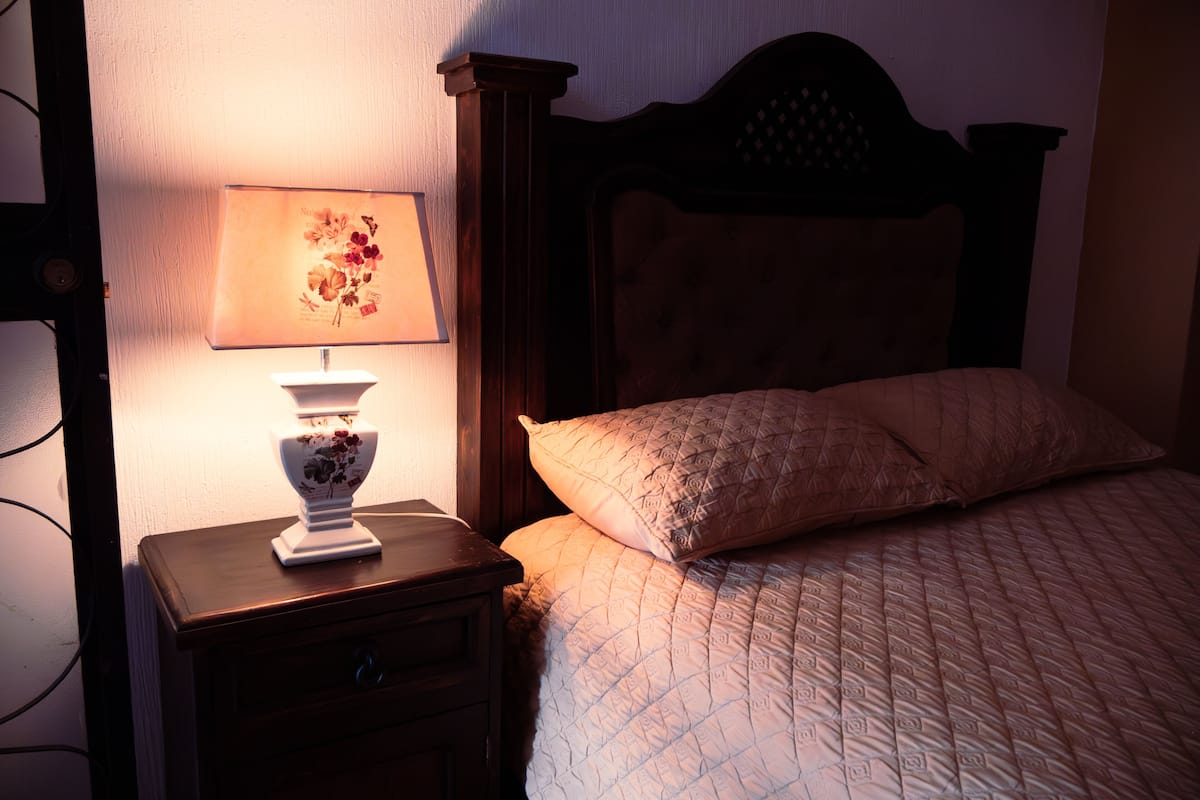 Un dormitorio con cabecera de madera, una mesita de noche con lámpara y colcha acolchada.