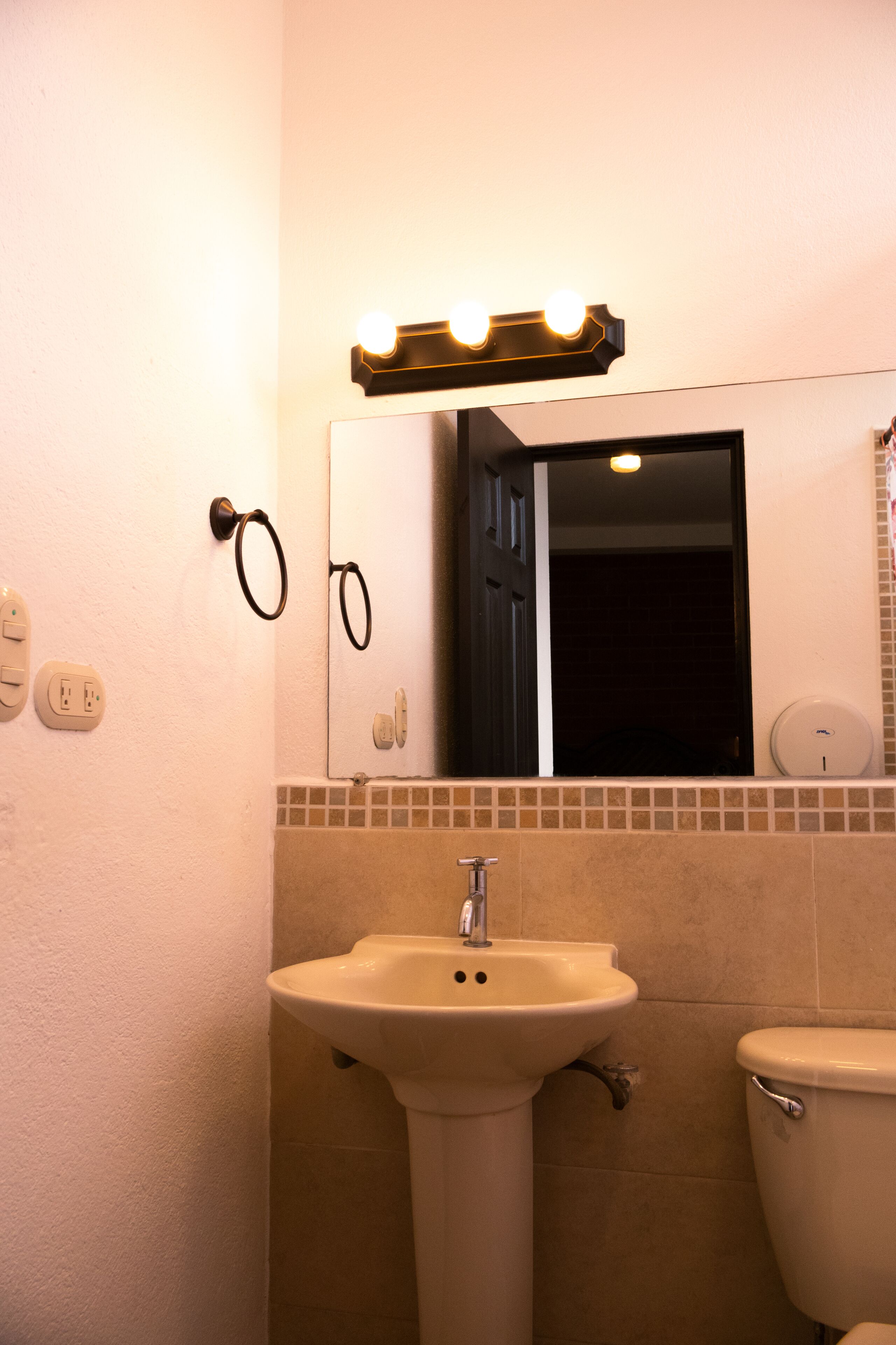 A bathroom with a sink, toilet, and a mirror with lights above.