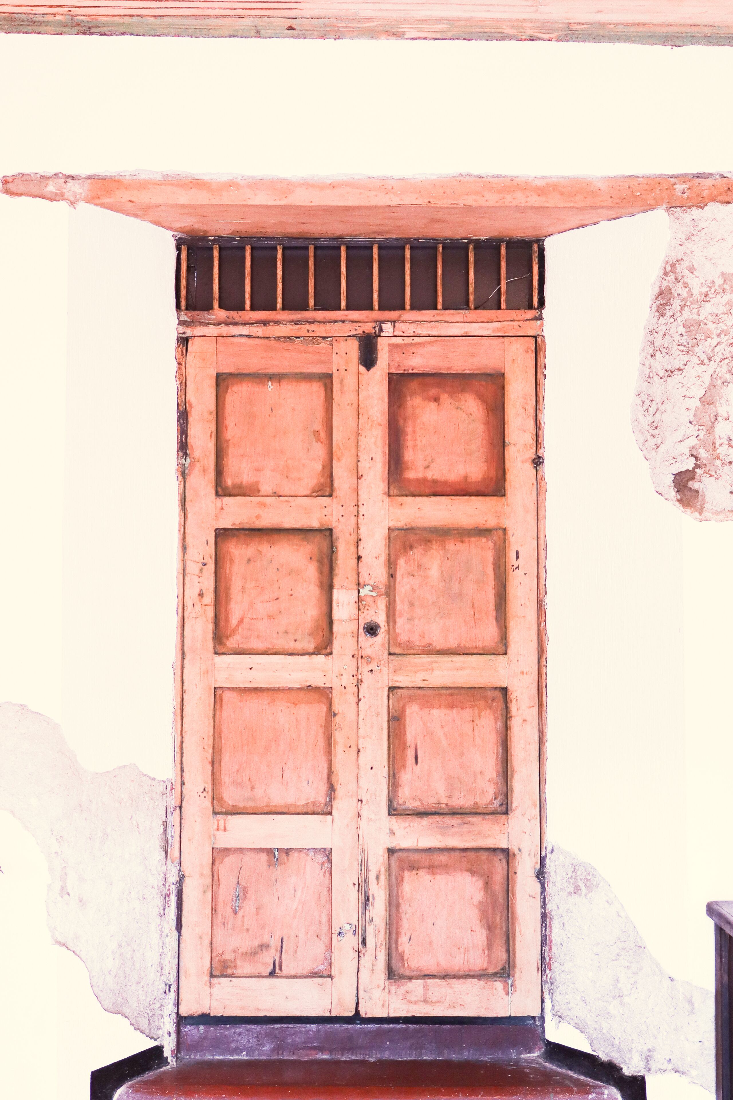 A wooden door with a metal grid above it, set against a plain wall.
