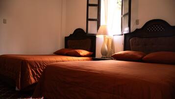 A room with two beds, each with a wooden headboard and matching pillows. There is a nightstand with a lamp between the beds.