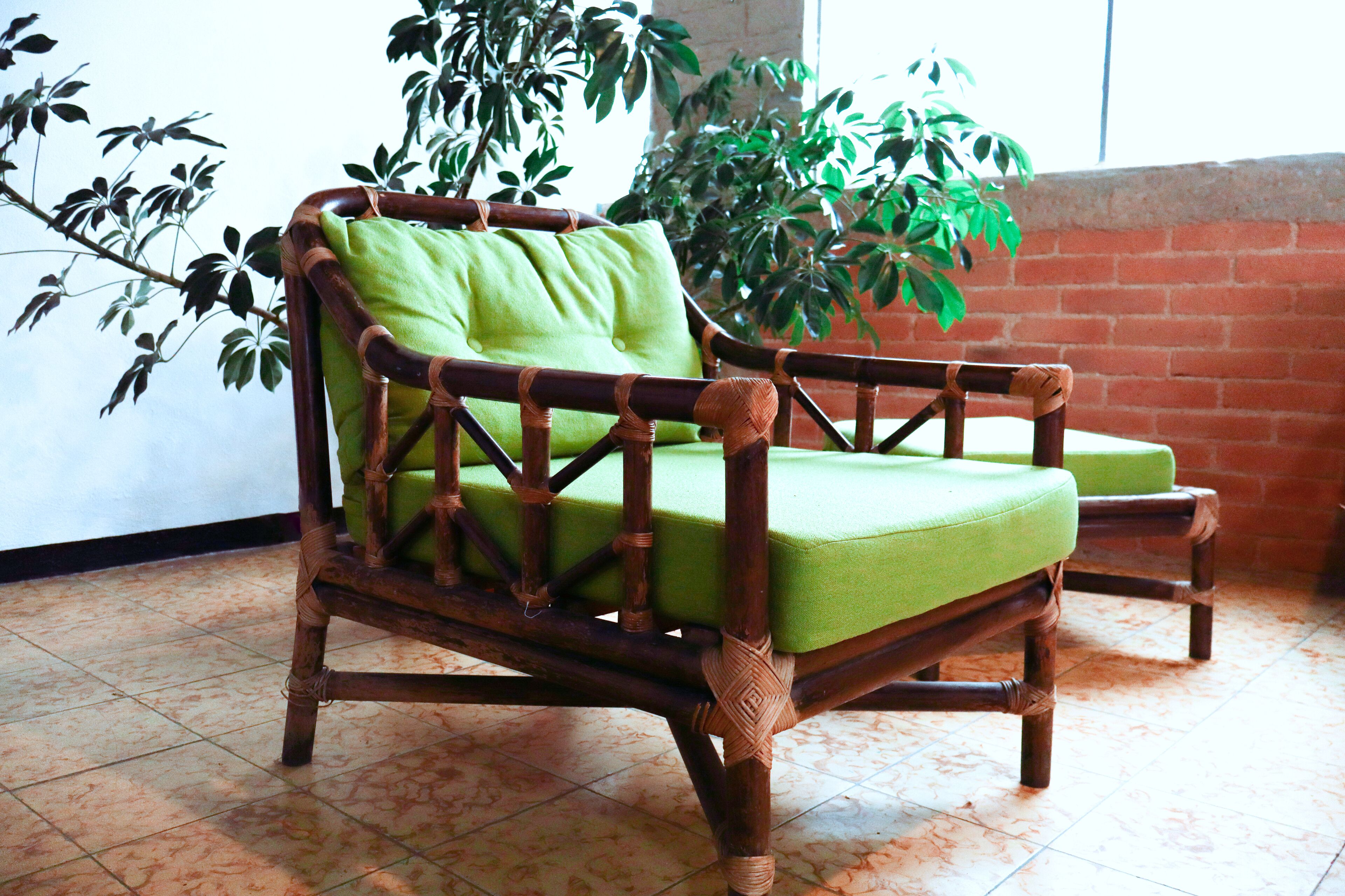 A wicker chair with a green cushion in a room with tiled flooring and a brick wall.