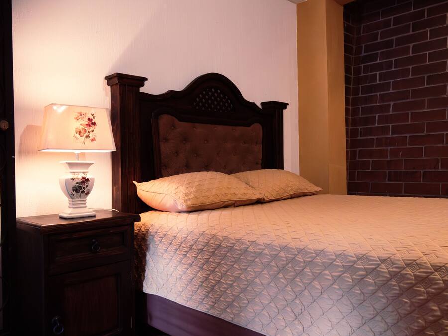 A neatly made bed with a quilted cover, a wooden headboard, and a bedside table with a lamp.
