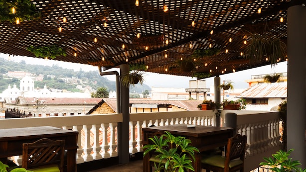 A terrace with wooden furniture and hanging plants, overlooking a cityscape with historical buildings. - Lar Antiqua Hotel (Quetzaltenango)