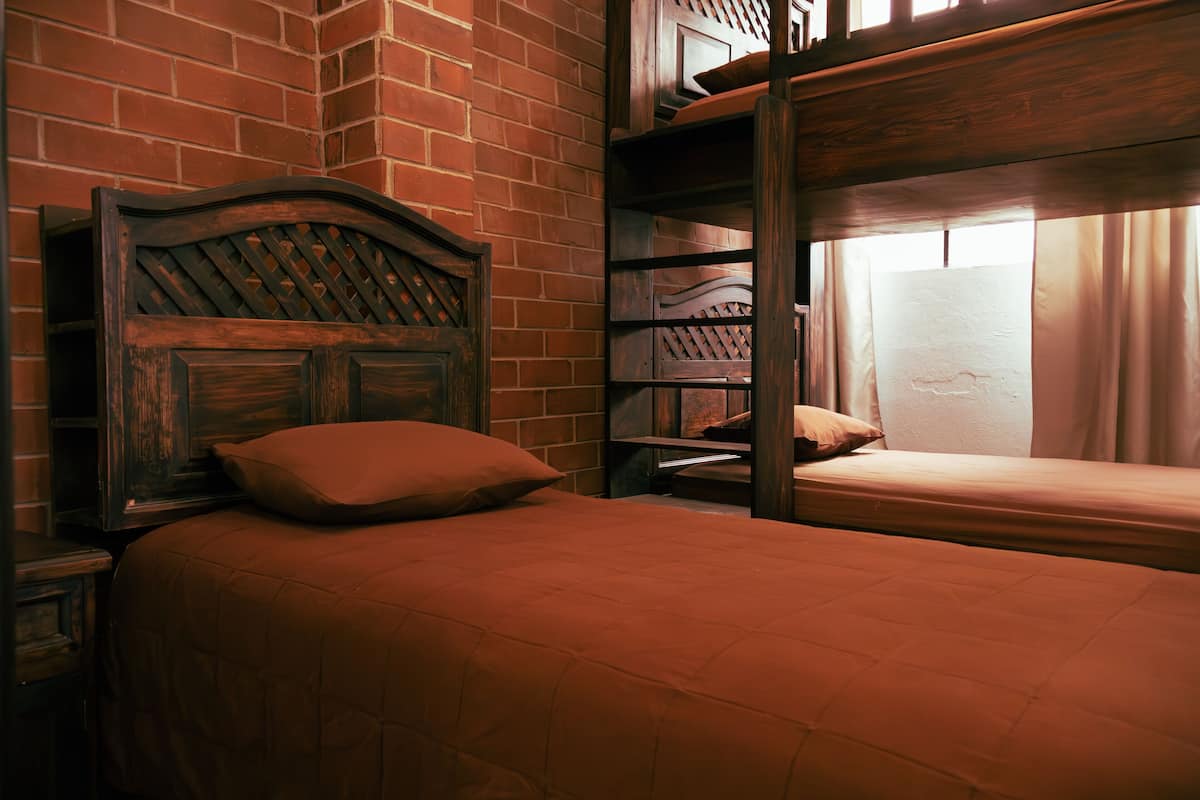 Una habitación con una cama de madera, una mesita de noche y una pared de ladrillo.