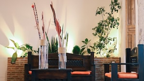 A cozy seating area with a wooden ceiling, a tiled floor, and a brick wall. There are two chairs with orange cushions and a small table with a basket. - Lar Antiqua Hotel (Quetzaltenango)
