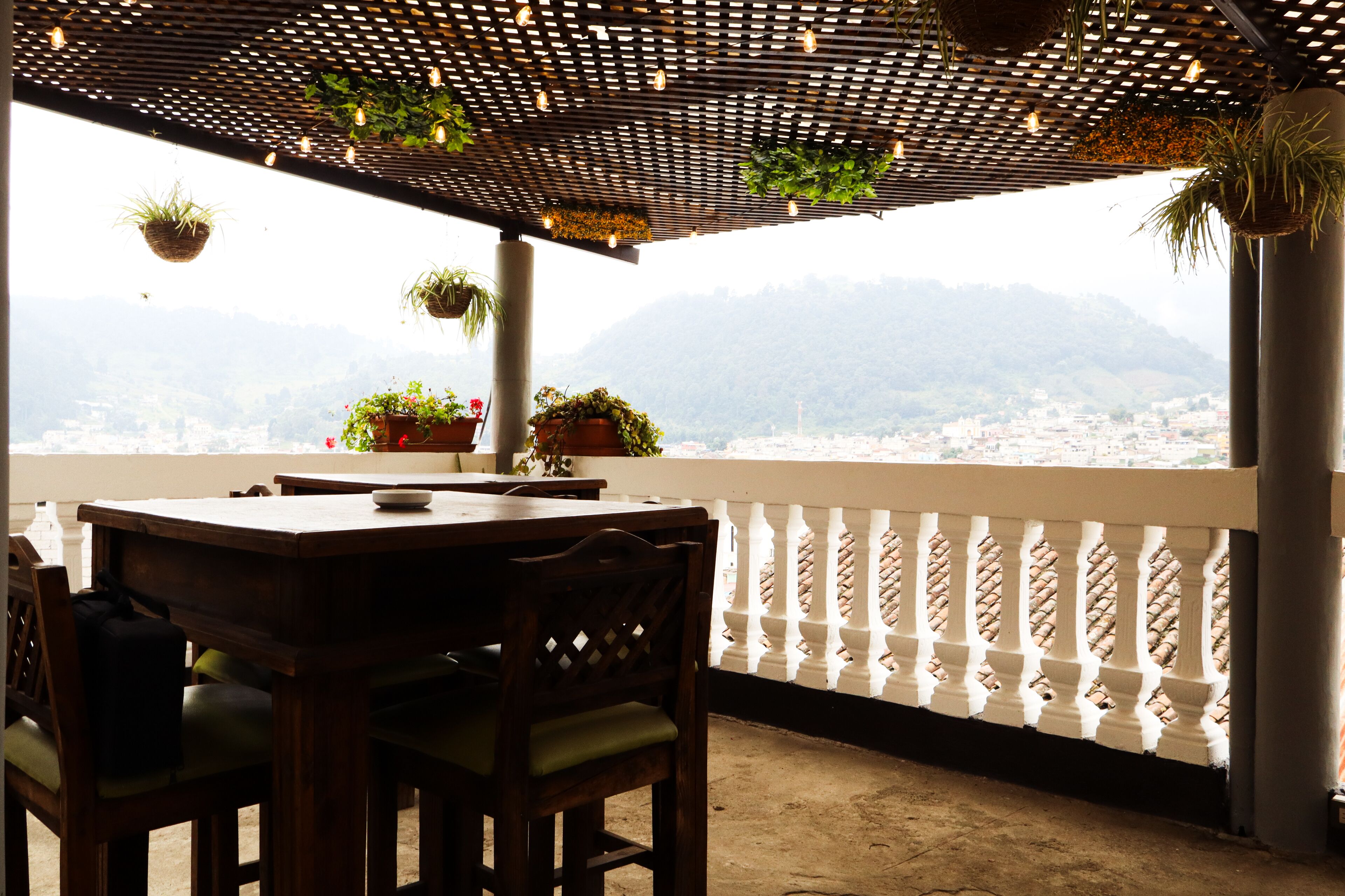 Un balcone con tavolo e sedie, piante in vaso e vista sulla città e sulle montagne.