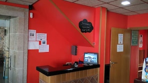 A reception desk with a red wall, a blackboard with a welcome message, and a computer monitor displaying a building image.