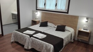 A double bed with a headboard, two bedside tables, a small bedside plant, and a window with curtains.
