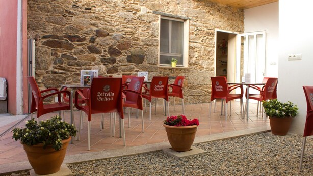 Un espacio al aire libre para comer con paredes de piedra, sillas y mesas rojas, plantas en macetas y una ventana con vistas.