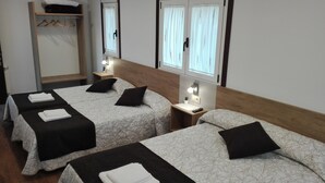 Una habitación de hotel con dos camas, cada una con colcha de diseño blanco y negro, una mesita de noche con lámpara y un armario con ropa colgada.