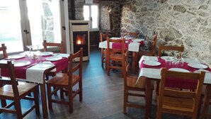 Un comedor con mesas y sillas de madera, paredes de piedra y una chimenea.
